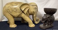 Pair of two elephant statues together: large beige composite resin elephant and smaller dark elephant figurine with bowl.