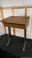 Full view of vintage wooden school desk with hinged top and black metal legs.
