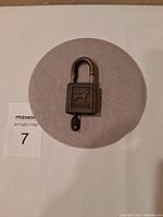 Top-down photo showing vintage POLICE PUP padlock with key on a light grey circular mat.
