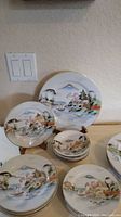 Photo showing stacks of dinner plates, luncheon plates, small bowls, and butter plates painted with Asian landscapes and gold trim.