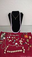 Full overview of the costume jewelry lot on a red cloth with necklaces displayed on a black jewelry display stand.