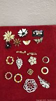 Full view of all 19 vintage costume jewelry pins and brooches arranged on a red fabric background
