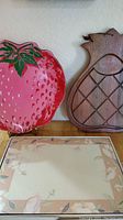 Photo showing the strawberry tray in red with green leaves, wooden pineapple carving board with crisscross pattern, and single English Life Nouveau Rose placemat with floral pattern.