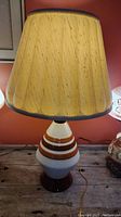 Full view of the vintage ceramic textured and glazed table lamp with beige fabric tapered shade on a wooden surface.