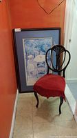 Full view of framed wall art titled 'Boston Public Garden' by Maurice Prendergast next to an antique chair with red velvet seat cover.