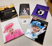 Five books laid out facing upward showing covers with images of Queen Elizabeth II and Downton Abbey.