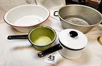 Four pieces including small white enamelware pot with lid, drab avocado green pot, large white enamelware dish pan with red rim, and silver metal pan with handles