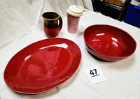 Photo of Ayesha Curry maroon bowl and oval platter, Longaberger pink travel mug with lid, and large ceramic mug on white sheet backdrop.