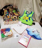 Overview photo of all baby items including diaper bag, swimming vest, bath toys, security blanket, DVD, hat, and photo holder.