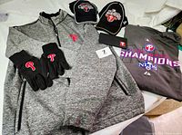 Overview photo showing all items in the lot including jacket, T-shirt, hats, gloves, and checkbook cover with Phillies logos