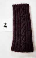 Front view of the purple hand-knitted headband displaying the single cable knit pattern down the center against a white background with item number card.