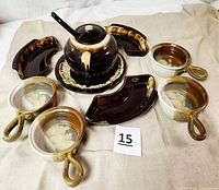 Full set of stoneware soup tureen with lid, ladle, plate, four soup bowls, three crescent serving dishes arranged on cream cloth.