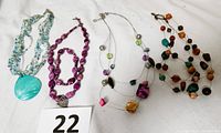 Four necklaces and one matching purple stretch bracelet displayed on a white background, showing variety in bead colors and styles.