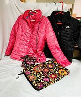 Photo showing the pink Izod jacket, black The North Face jacket, a colorful flower design cross-body bag, and a matching colorful flower design computer bag on a white backdrop.