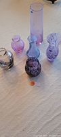Group photo showing six artisanal Caithness Glass vases of various shapes and purple hues on beige surface.