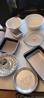 Selection of various cake and pie pans including metal, silicone, and glass materials shown arranged on a table.