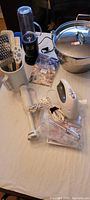 Full lot on table including canning pot with lid, ceramic jug with spatulas and metal grater, Oster hand mixer with beaters and manual, Magic Bullet blender, Braun immersion blender with accessory cup.