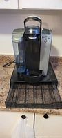 Keurig coffee maker with water reservoir on kitchen counter and pod holder drawer below