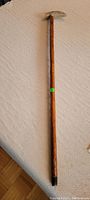 Full-length photo of the wooden walking stick showing wood shaft and white handle with black tip on the bottom.