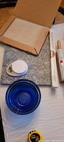 Photo showing white digital kitchen scale, three nested blue mixing bowls, marble pastry board, French rolling pin in original packaging, and rectangular baking stone.
