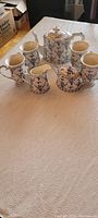 Full tea set arranged on beige cloth, showing four coffee cups, one teapot, one sugar bowl, and one creamer jug in blue floral porcelain.