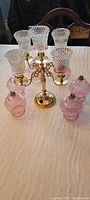 Brass table candelabra assembled with 5 hobnail cut glass candle holders and surrounded by 5 pink glass interchangeable candle holders on a tabletop.
