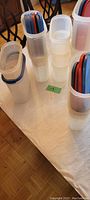 Multiple clear plastic Tupperware pantry storage containers with blue, red, and white lids on table