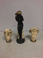 Three composition Art Deco figures including a black nude figure flanked by two head sculptures on a tabletop.