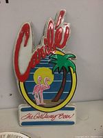 Front view of Caribe shaped plastic beer advertising sign with flamingos, palm tree, and sunset design