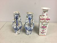 Full view of three Chinese porcelain vases showing the pair of blue and white fertility vases with sculpted children and the floral rectangular vase.