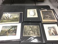 Overview photo showing multiple unframed prints and engravings displayed on black portfolio pages including landscapes and classical figures.