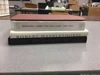 Side view showing spines of three of the four art books, titles visible for Alexander Calder, Robert Mapplethorpe, and Richard MacDonald books.