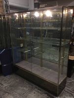Front and full view of the glass display case showing metal frame, glass shelves and lighting on top.
