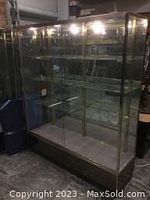 Full frontal view showing the glass display case with metal framing and lighting at the top, with visible three glass shelves and mirrored back panel.