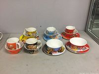 Photo of 9 Kellogg's porcelain dishes featuring bowls, plates, and mugs with Frosted Flakes, Rice Krispies, and Corn Flakes cereal designs arranged on a flat surface and shelf.