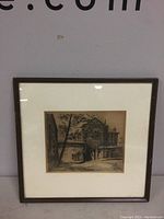 Framed etching of village street mounted and hanging, showing entire piece with frame