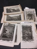 Group of unframed etchings and engravings showing scenic views and figures, some with ornate borders, in loose folios, laid on black surface.