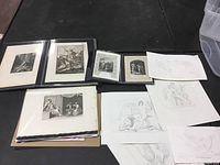 Photo showing multiple folios containing unframed black and white engravings, prints, and book pages, some with descriptive text