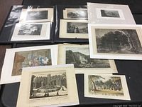 Photo of multiple unframed engravings and prints laid flat on a dark surface, including both black and white and colored pieces.