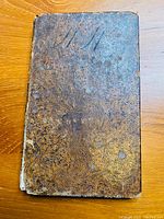 Front cover of a small, worn, leather-bound book showing significant wear and age marks.