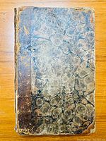 Front view of the antique book showing the worn leather spine and marbled paper covers with heavy wear and fading.