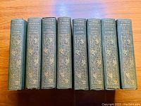 Photo showing the spines of all 8 hardcover volumes in green cloth with gilt floral spine decoration and text.