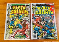 Photo showing front covers of Black Goliath issues #2 and #3 comic books side by side on wooden surface.