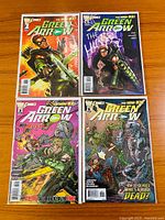 Four Green Arrow comic books laid out flat on wooden surface showing front covers with vibrant action artwork and titles.