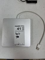 Top-down view of the Apple SuperDrive showing the label with lot information and USB cable attached.