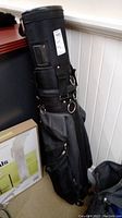 Full view of the black golf bag standing upright, showing the overall shape and construction with attached wheels.