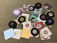 Overview image showing scattered 7-inch vinyl records with various colorful center labels and original paper sleeves on carpet.