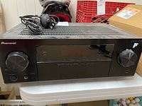 Front view of black Pioneer AV receiver VSX-532 showing the input selector knob on the left, central display, control buttons, and wired remote sensor cable coiled on top.