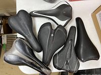 Six black bicycle seats placed on a white table top, visible brands include Giant Connect, Body Geometry, Reebok, and Vetta.