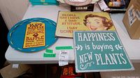 Photo of two metal signs and one metal tray on a table. Shows text details and condition with light scratches.